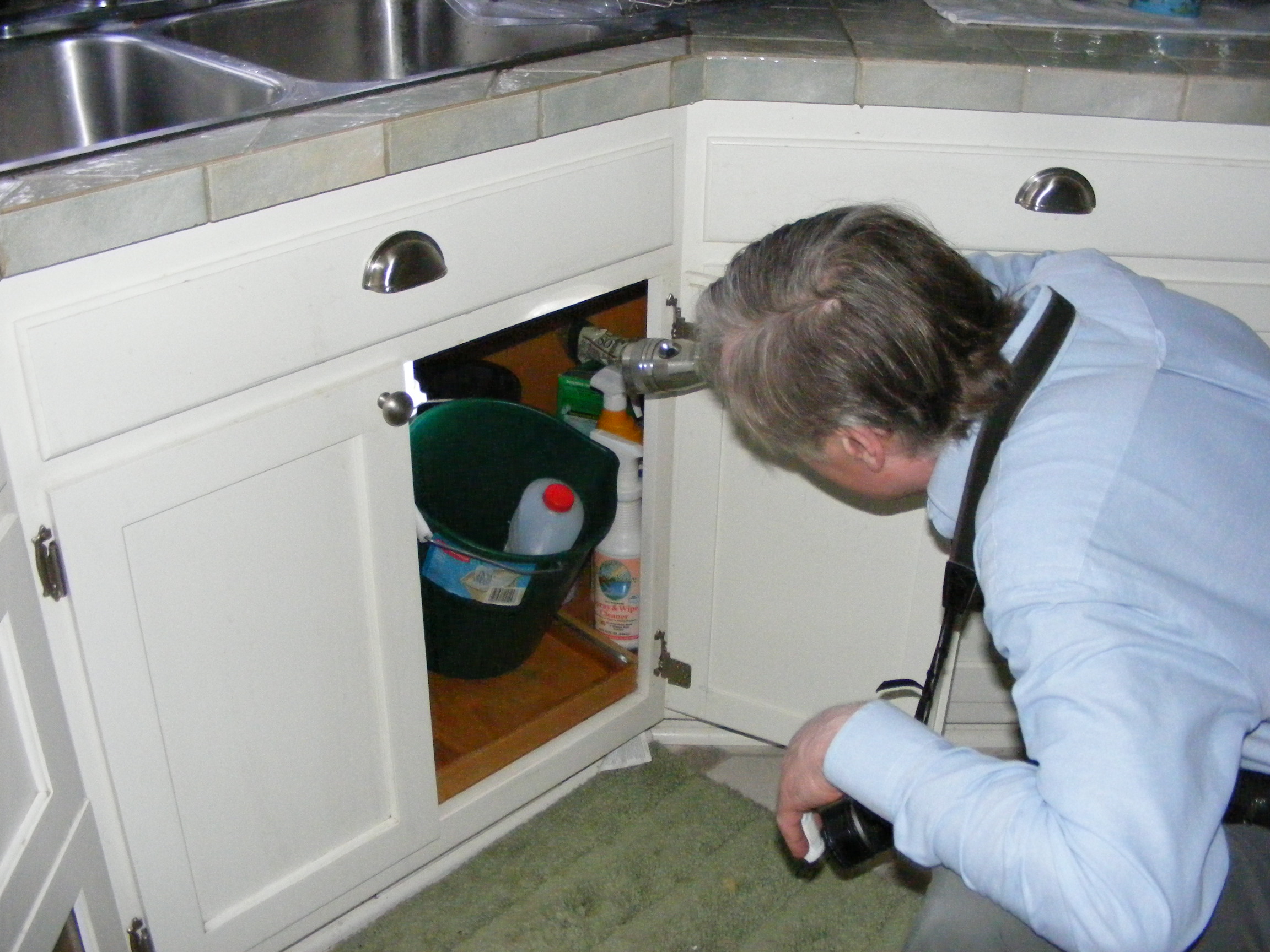 Charles Buell inspects under a kitchen sink Photo